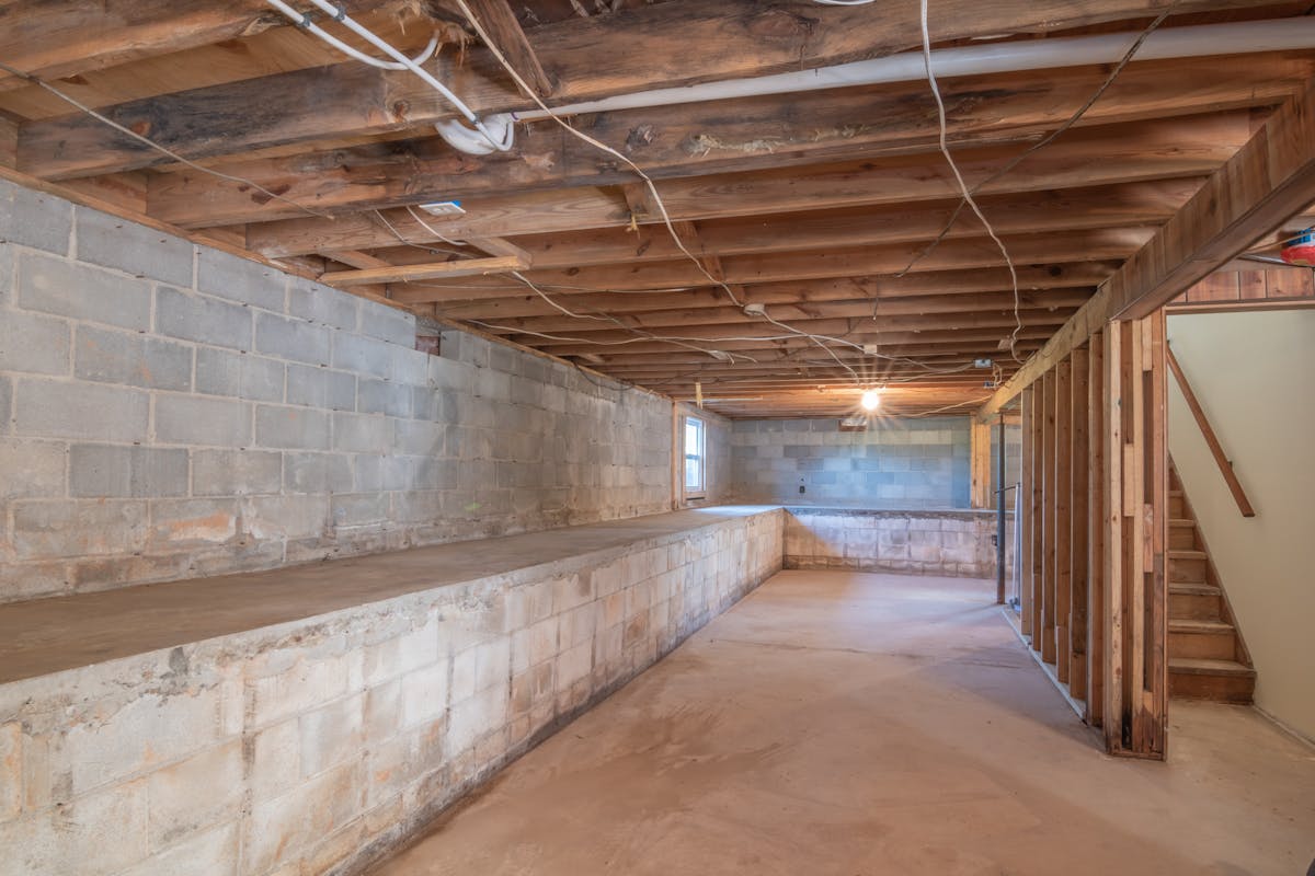 Empty basement with exposed wooden beams and concrete walls in a Hoboken home ready for waterproofing